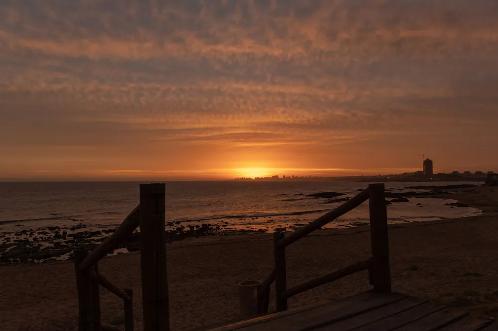 Atardecer en la playa de La Barra, Maldonado, con la costa rocosa y el perfil urbano de fondo