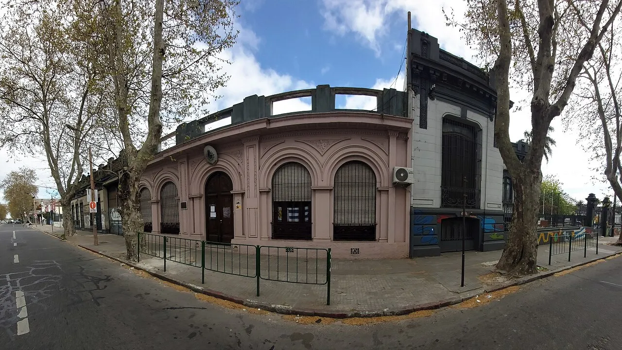 Antigua edificación de esquina de estilo ecléctico, con arcos y balaustrada, sobre una avenida arbolada en Jacinto Vera, Montevideo