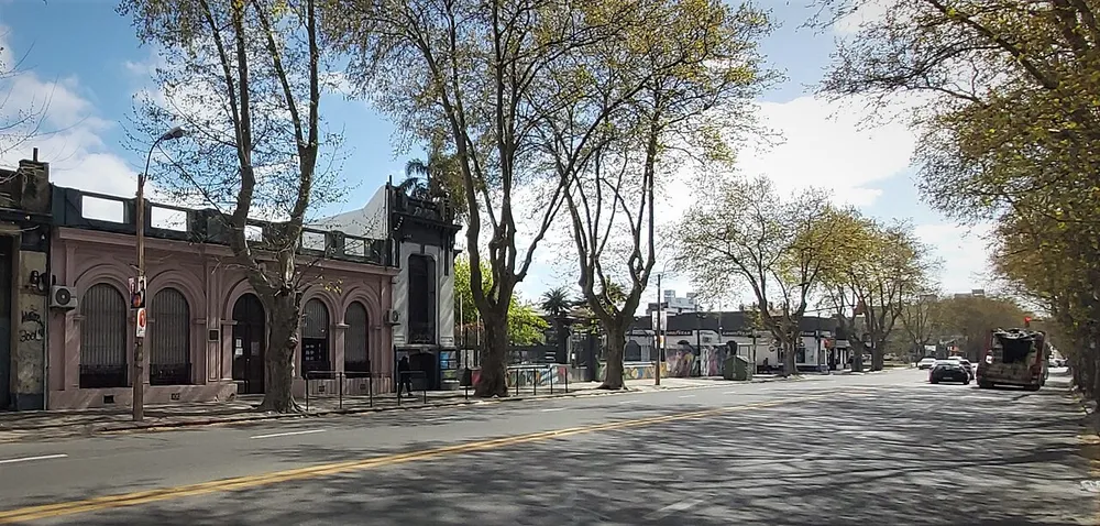 Avenida arbolada de Jacinto Vera con el edificio histórico de esquina —el mismo de la imagen destacada, visto aquí de lejos y en plano general— integrado a la fisonomía de casas bajas y arbolado del barrio