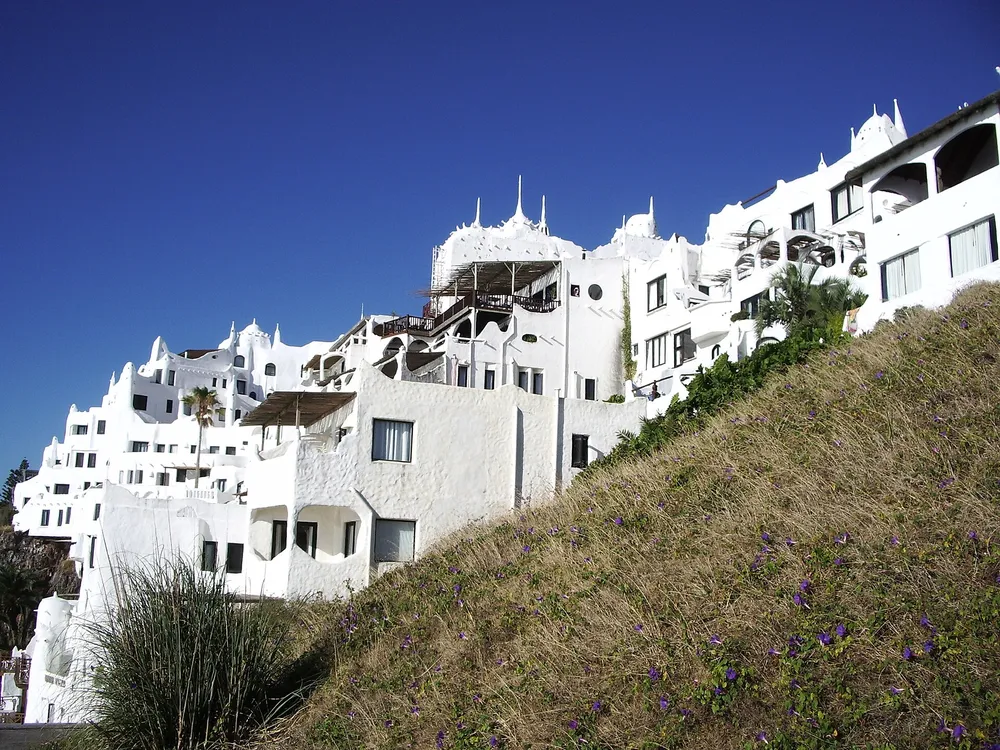 Fachada blanca y curva de Casapueblo en Punta Ballena, con flores silvestres en primer plano.