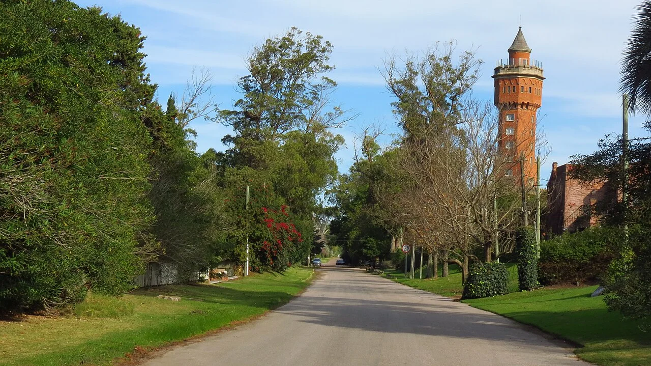 Calle arbolada en el barrio Golf, Punta del Este, con la antigua Torre del Agua integrada al Hotel L'Auberge al fondo